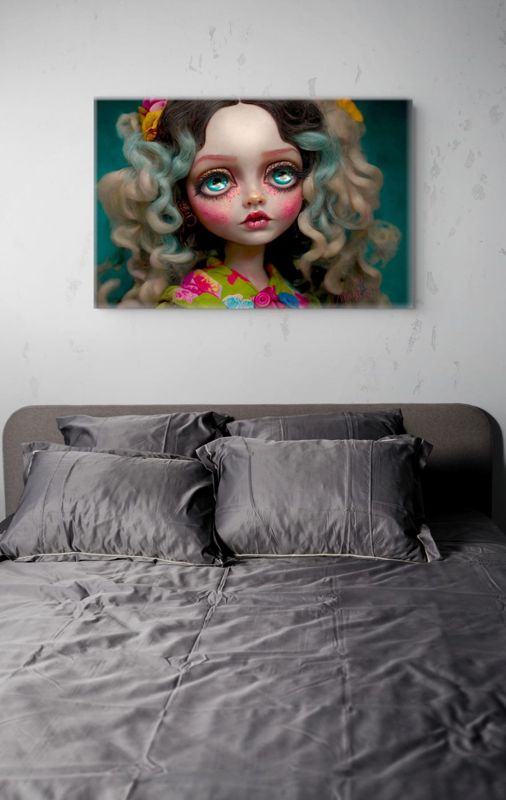 The teal eyed doll portrait canvas hung on a pale plaster wall above a bed with charcoal grey linen.