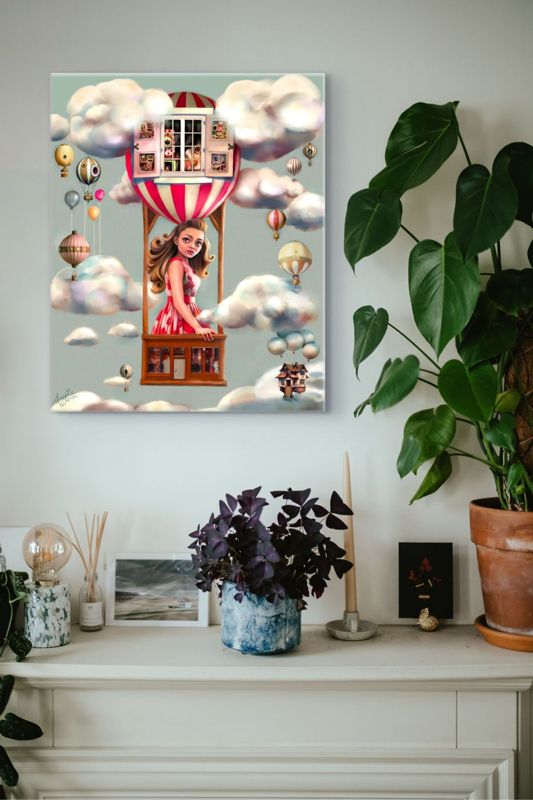 The hot air balloon girl canvas hung on a white wall above a white mantel crowded with houseplants and small frames.