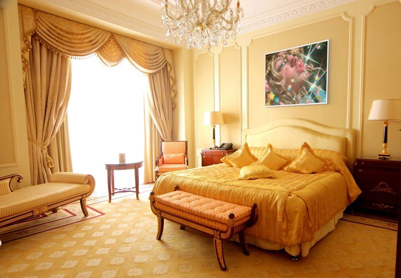 The rainbow sparkle girl print hung in a warm gold bedroom with a crystal chandelier, yellow bedding and tall curtained windows.