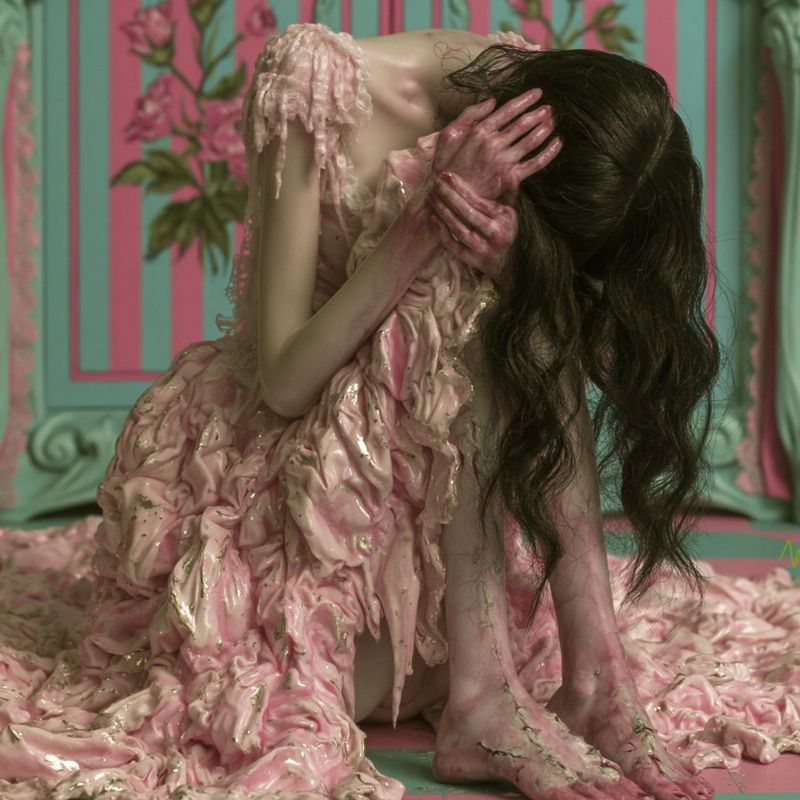 Closer view of the kneeling figure, head bowed, hands in her dark hair, the melting pink dress spreading across the floor.