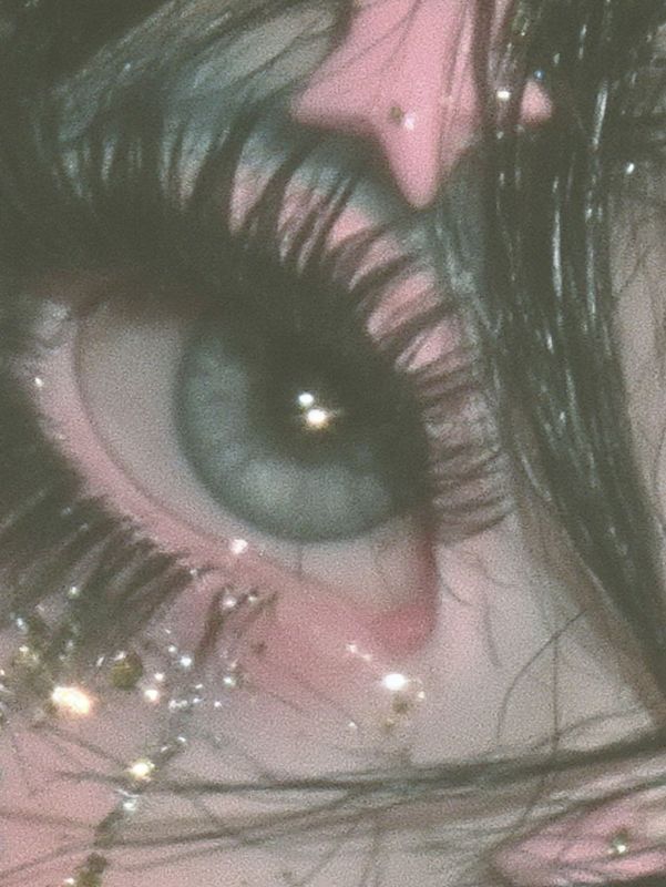 Close up detail of one huge grey blue eye with long lashes, glitter and tiny gold stars falling from it, a pink star clip above.