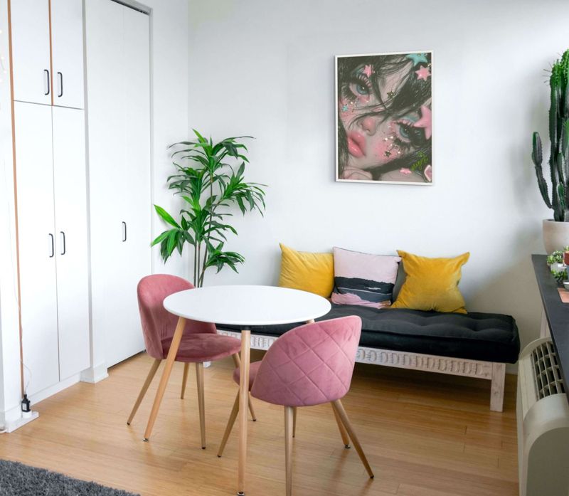 The star face print hung on a white wall above a small round dining table with pink and grey chairs and a black bench.