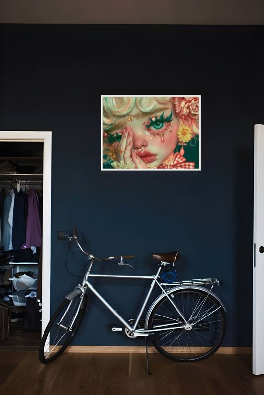 The crying clown doll print hung on a navy wall above a vintage bicycle beside an open wardrobe.