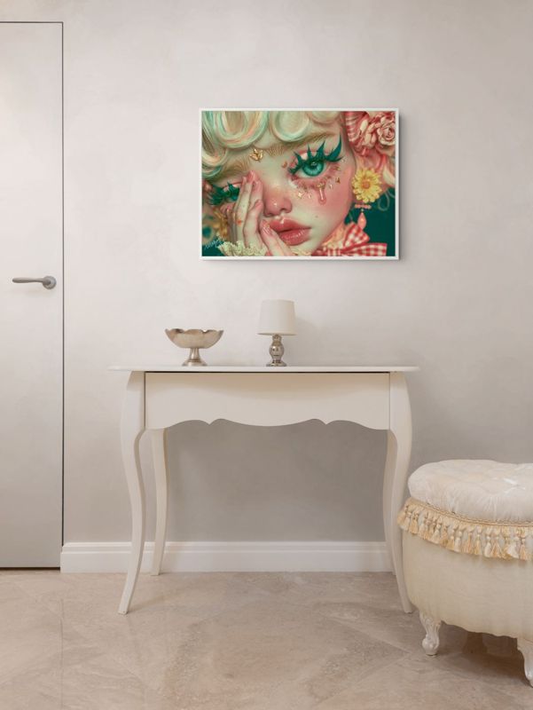 The crying clown doll print hung on a pale wall above a white French console table with a small lamp and a tasseled ottoman.