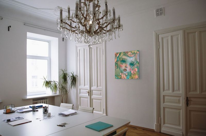 The crying doll print on the white wall of a grand room with a crystal chandelier, tall paneled doors and a long white table.