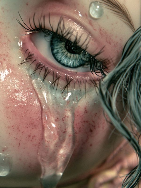 Extreme close up of a pale blue eye with wet lashes and a thick glassy tear sliding down a freckled pink cheek beside dark wet hair.