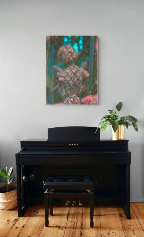The teal and pink print of a figure behind a chain link fence hung on a pale grey wall above a black upright piano with a plant, warm wood floor.