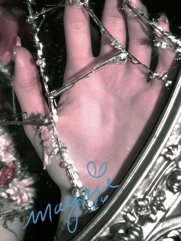 Detail of a hand pressed flat against cracked mirror glass beside the ornate silver frame, with the blue Magpie signature.