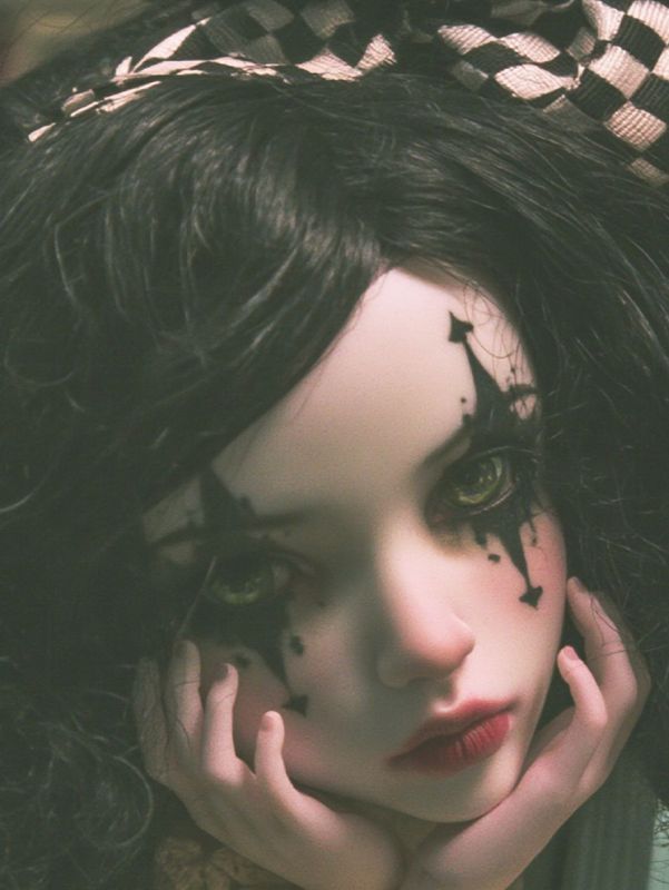 Close up detail of the doll's face: black diamonds painted under her eyes, dark lips and her cheek resting in her hand.