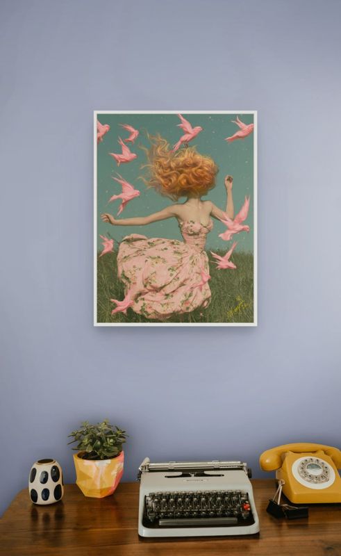 The girl with pink birds print hung on a grey wall above a mid century desk with a cream typewriter and yellow rotary phone.