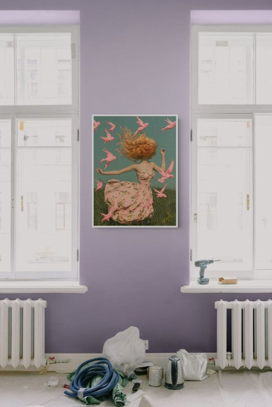 The girl with pink birds print hung on a lavender wall between two tall white windows with a radiator below.