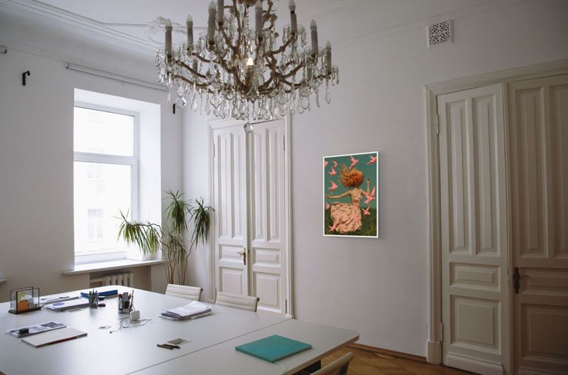 The girl with pink birds print hung in a bright white room with a crystal chandelier and tall paneled doors.