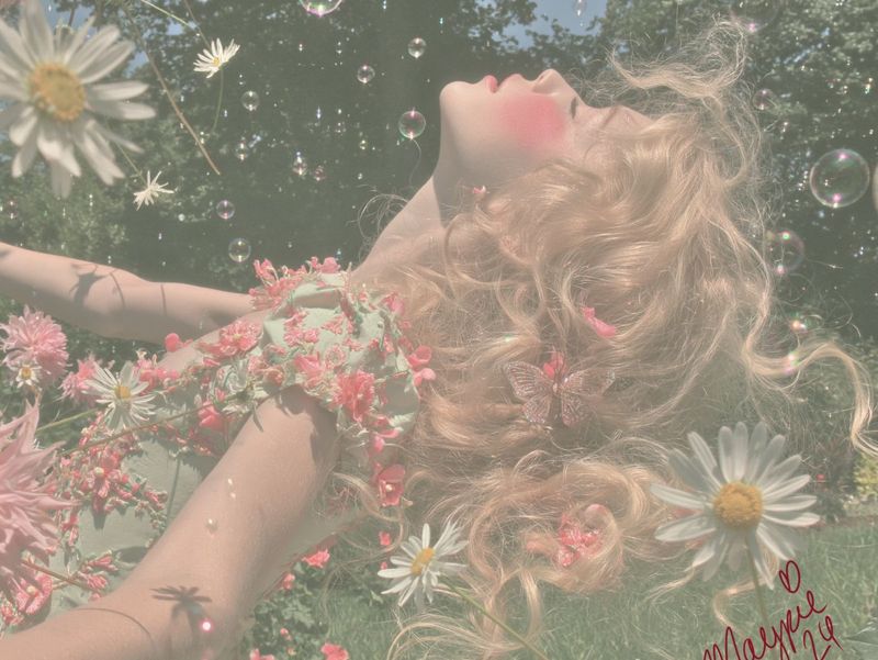 Closer view of the girl lying back among daisies and pink dahlias, face turned up, blonde hair spilling into the grass.