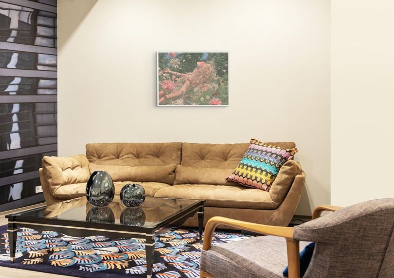 The girl in daisies print hung on a dark wall above a gold velvet sofa with a patterned rug and a low table.