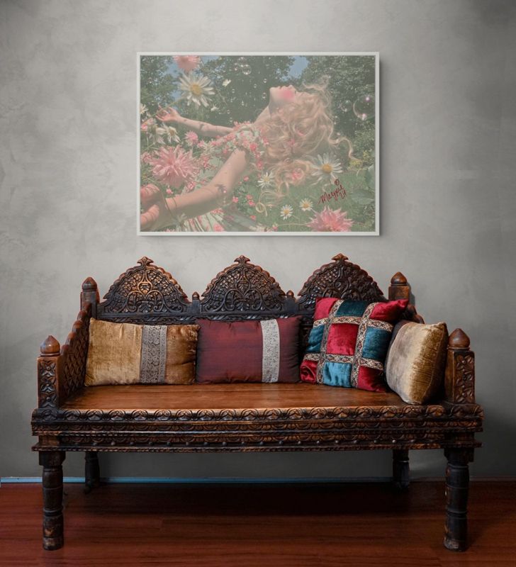The girl in daisies print hung above a carved wooden bench heaped with patterned cushions on a grey wall.