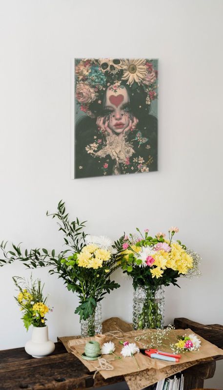 The skull and flower crown print hung on a white wall above a wooden table with a vase of yellow flowers.