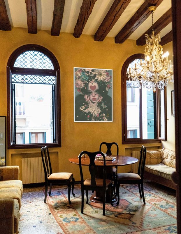 The skull and flower crown print hung in a warm yellow room with wooden beams, arched windows and a chandelier.