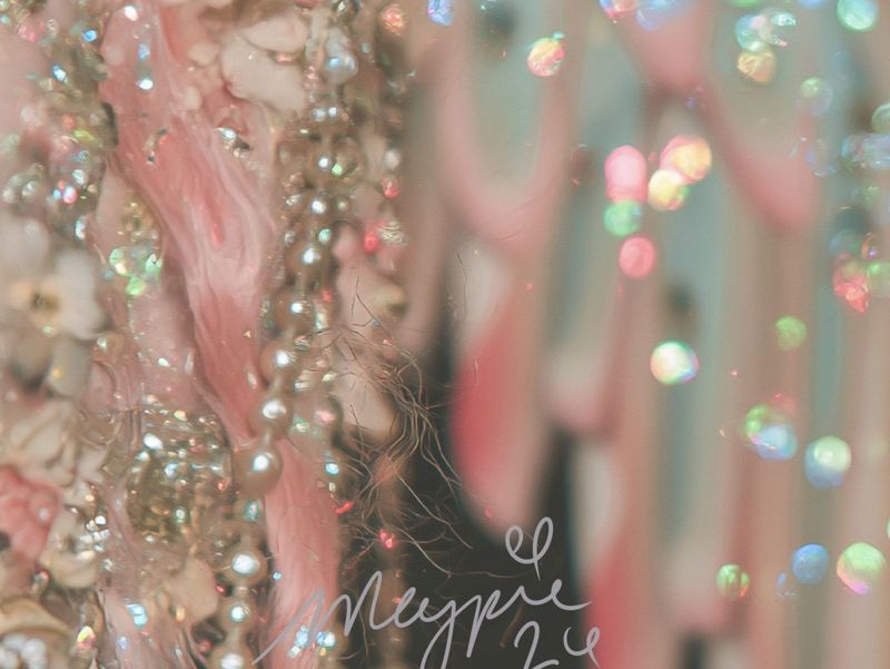 Close up of the lower right: glittering pink and white feathered wing dripping with sequins, with the Magpie signature in pale script.