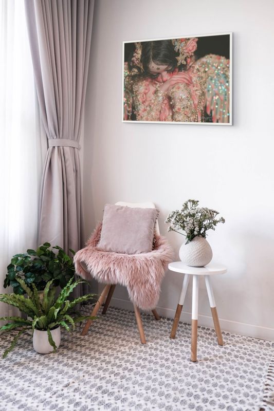 The weeping angel doll print hung on a grey wall above a pink fur chair with pale curtains and plants.