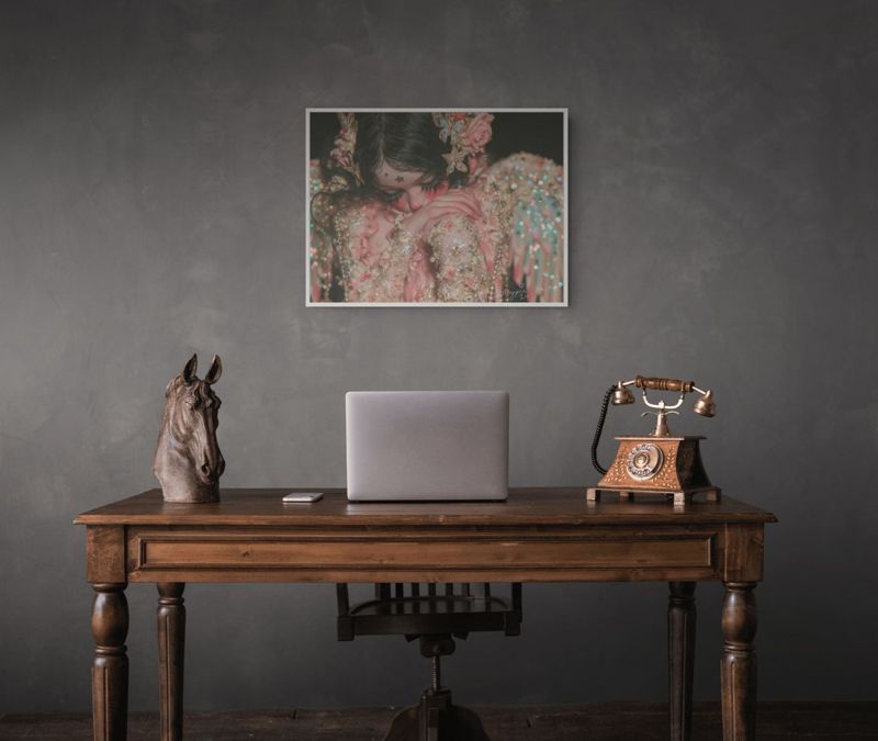 The weeping angel doll print hung on a dark grey wall above a wooden desk with a laptop and a rotary phone.