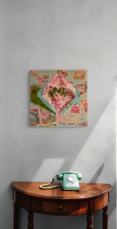 Square art print of a surreal doll in a vintage envelope displayed on a gray wall above a half-moon wooden table with a mint green rotary telephone.