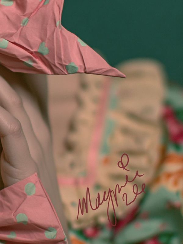 Close-up detail of a hand touching a pink polka-dot bow with teal dots, blurred cream ruffles and floral fabric behind, with the Magpie signature in dark pink script against a teal background.
