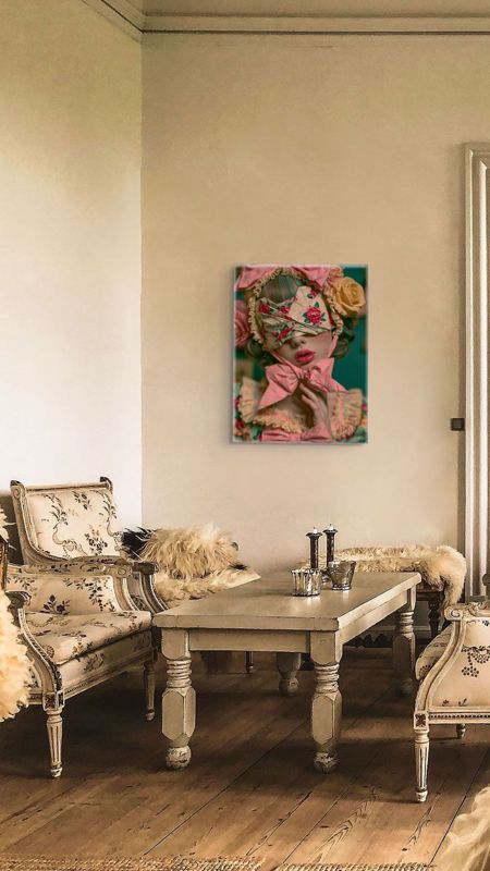 Portrait art print of a surreal blindfolded bow girl on a warm plaster wall between two cream floral Louis XV armchairs with sheepskin throws, above a rustic coffee table with silver vessels.