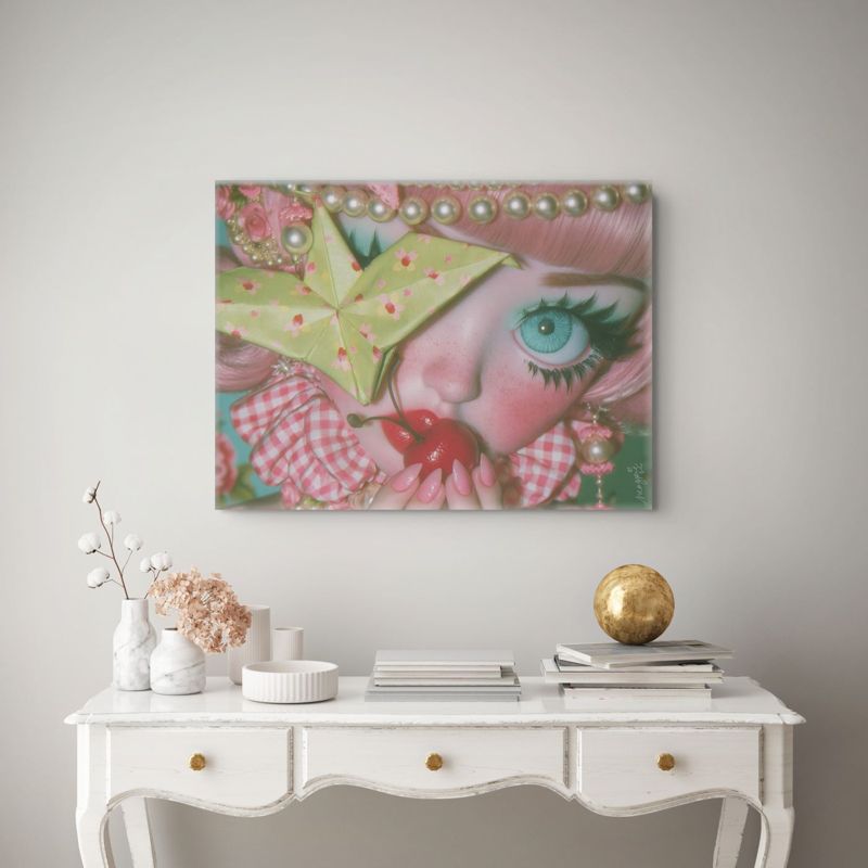 Landscape art print of a surreal big-eyed cherry girl on a warm gray wall above a white French writing desk with white vases, dried flowers, a gold sphere, and stacked books.