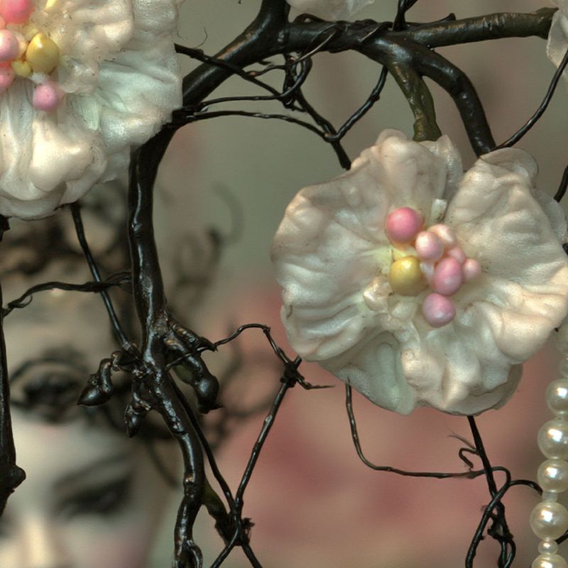 Close up detail of two white silk flowers with pink and yellow bead centers and a strand of pearls hanging from black wire.