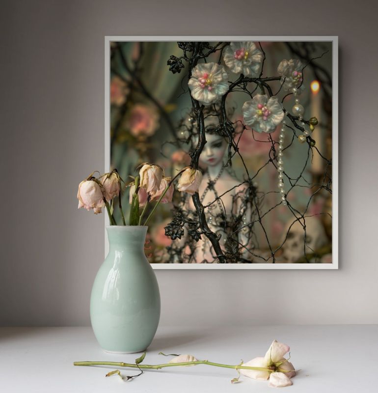 The wire branches and pearls print hung on a grey wall above a mint vase of wilting flowers on a white surface.