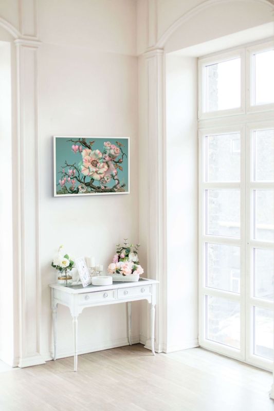 The flower doll on a branch print hung on a white wall above a white console table by a tall window.