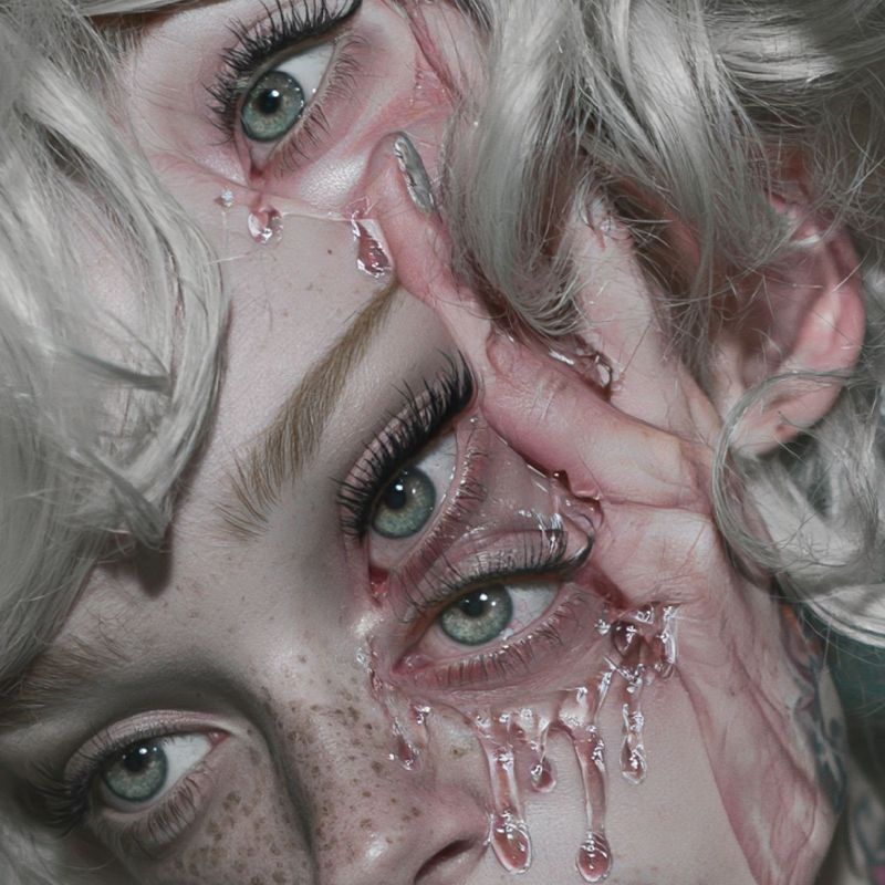 Close up detail of green eyes and the ghost of a hand fused into a freckled cheek, rose colored drips running down beside glossy lips.
