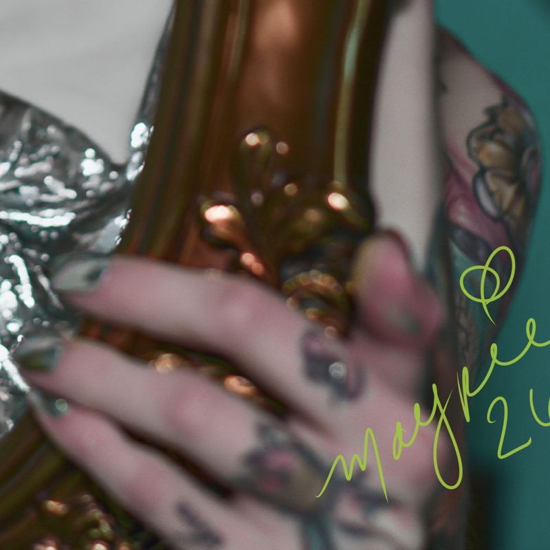 Close up of the lower right corner: a tattooed hand with silver nails gripping the carved gold frame with the Magpie signature in green script.