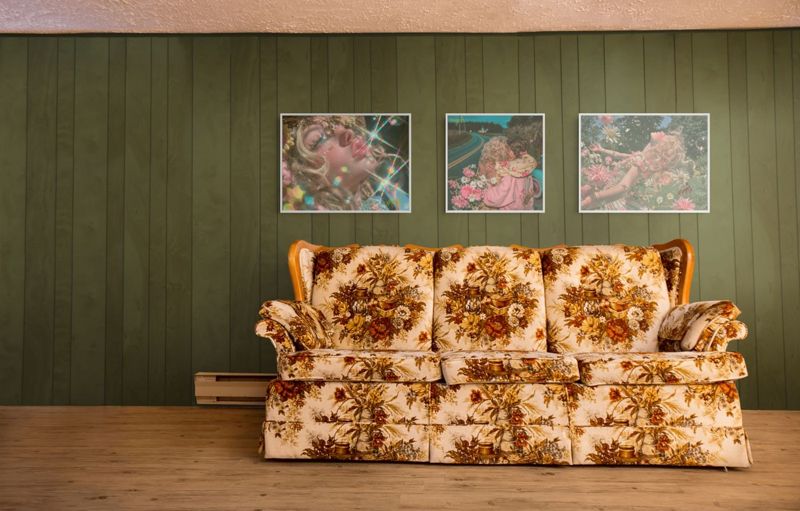 Three prints hung together on an olive green paneled wall above a floral sofa: the rainbow sparkle girl, the roadside hug and the girl in daisies.