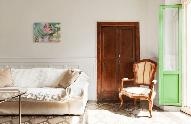 The mint hair girl print hung on a white wall above a cream sofa beside a bright green door.